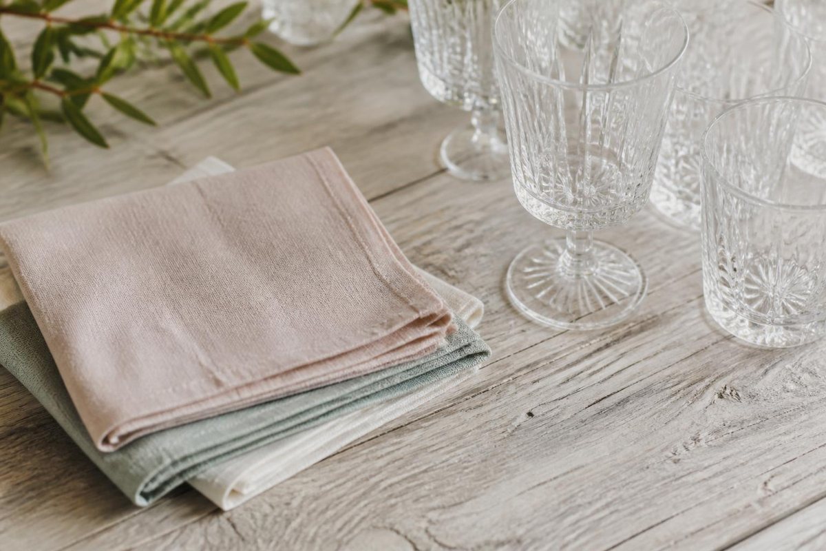 Folded blush, sage, and ivory napkins beside clear glasses