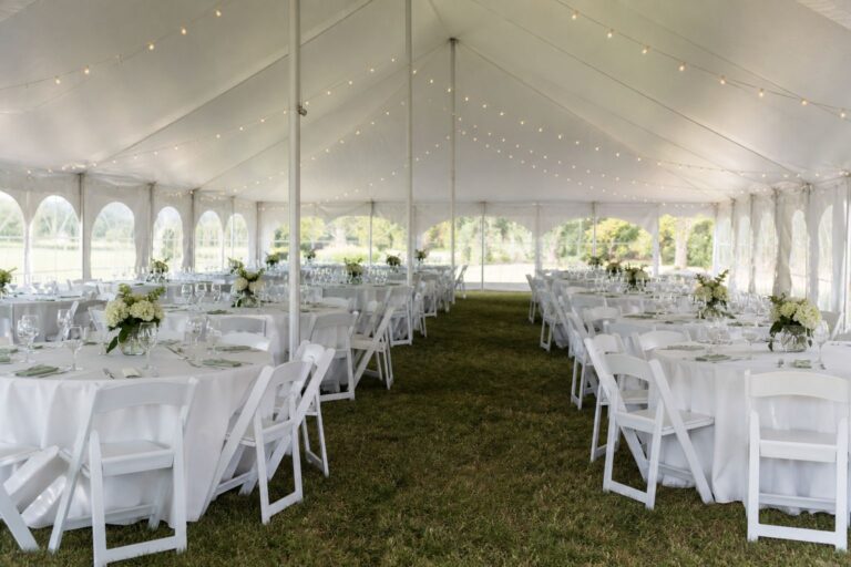 Large white tent with evenly spaced round tables, white folding chairs and a clear center aisle