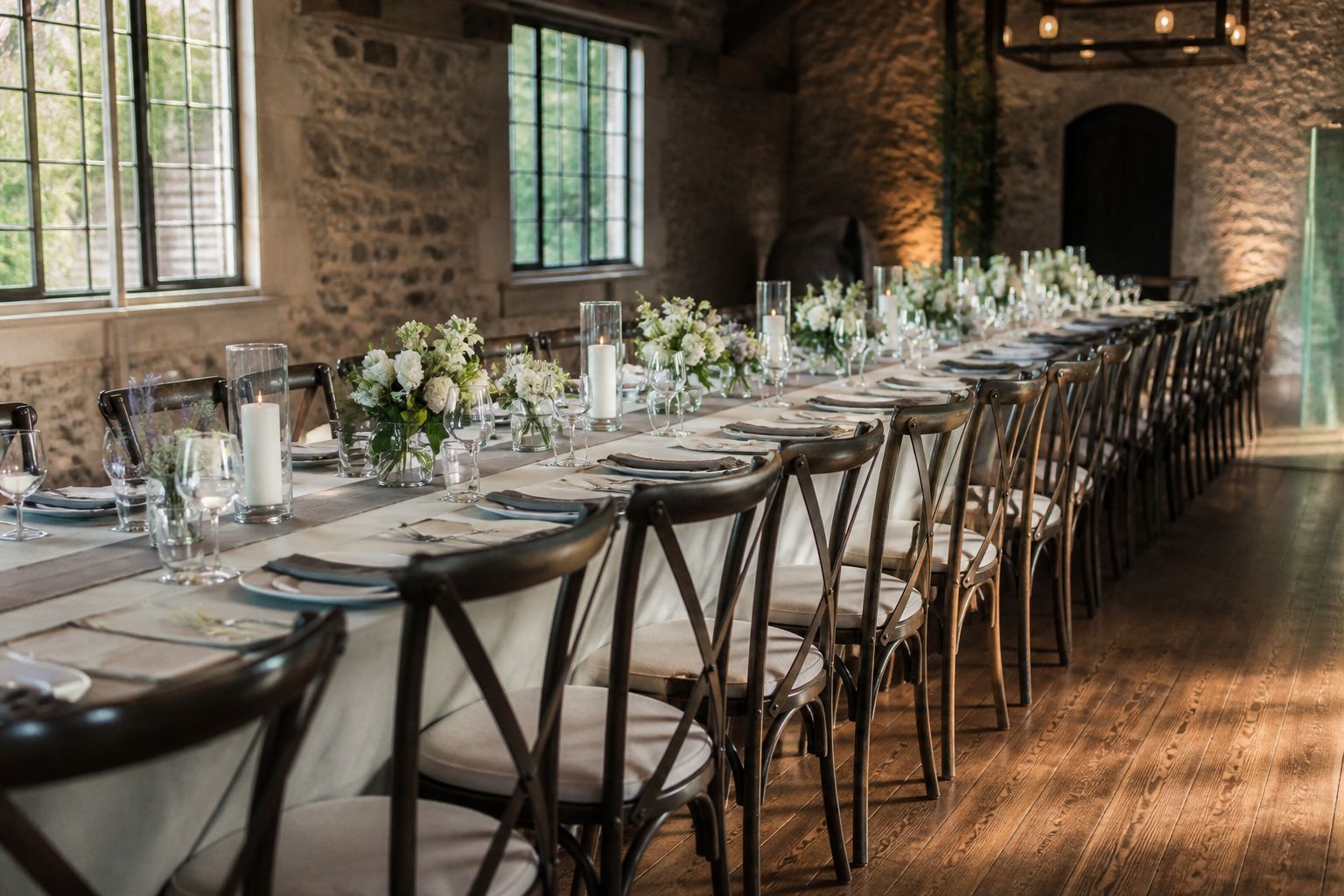 Long banquet table with a row of matching chairs and candles in a stone hall