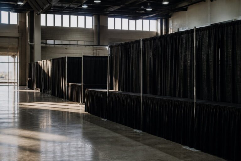 Rows of vendor booths divided by black pipe and drape in a large hall